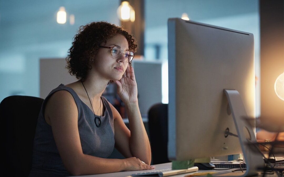 Woman looking thoughtfully at a computer screen in an office, symbolizing concern or confusion about missed open enrollment for health insurance.