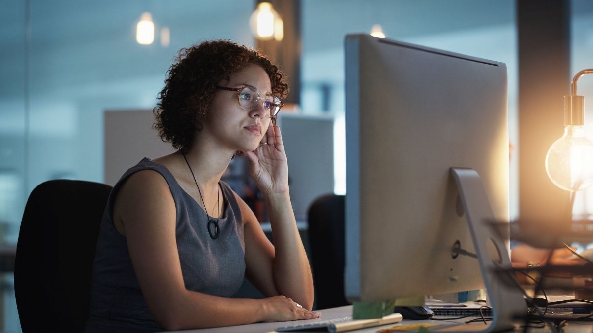 Woman looking thoughtfully at a computer screen in an office, symbolizing concern or confusion about missed open enrollment for health insurance.
