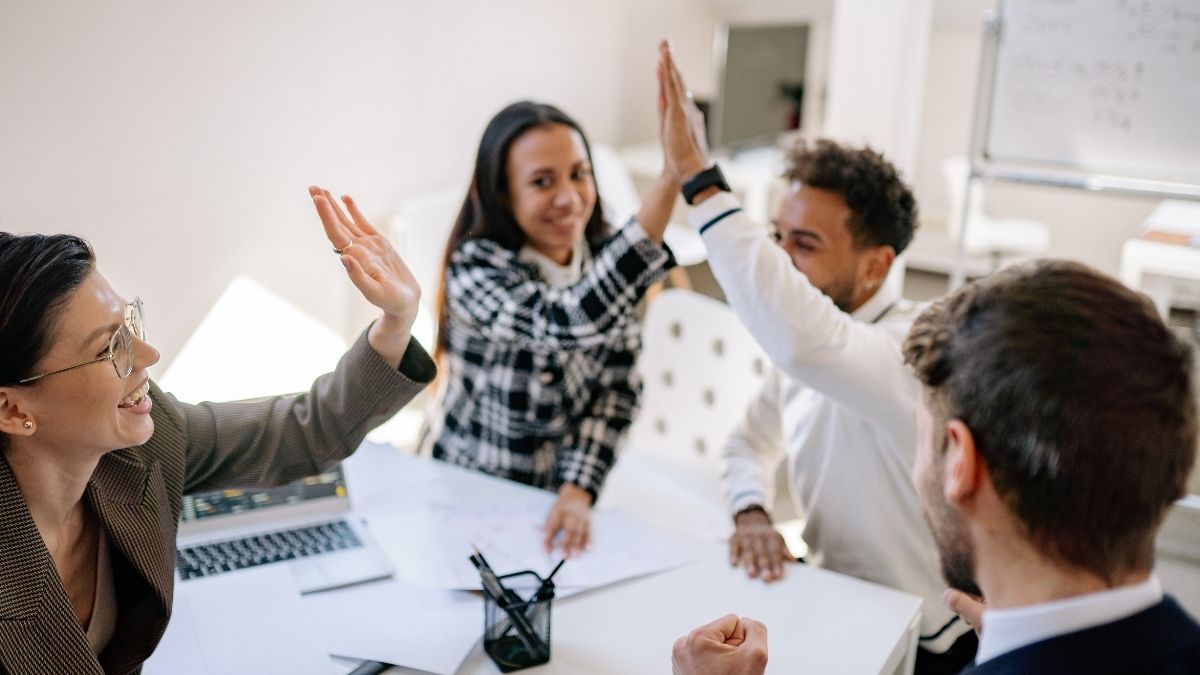 Happy coworkers high-fiving in a bright office, representing team satisfaction driven by top employee benefits.