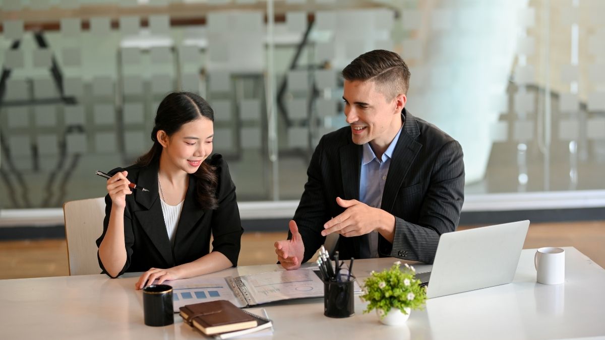 Two professionals discussing documents in an office, representing a conversation about what is the penalty for not having health insurance.