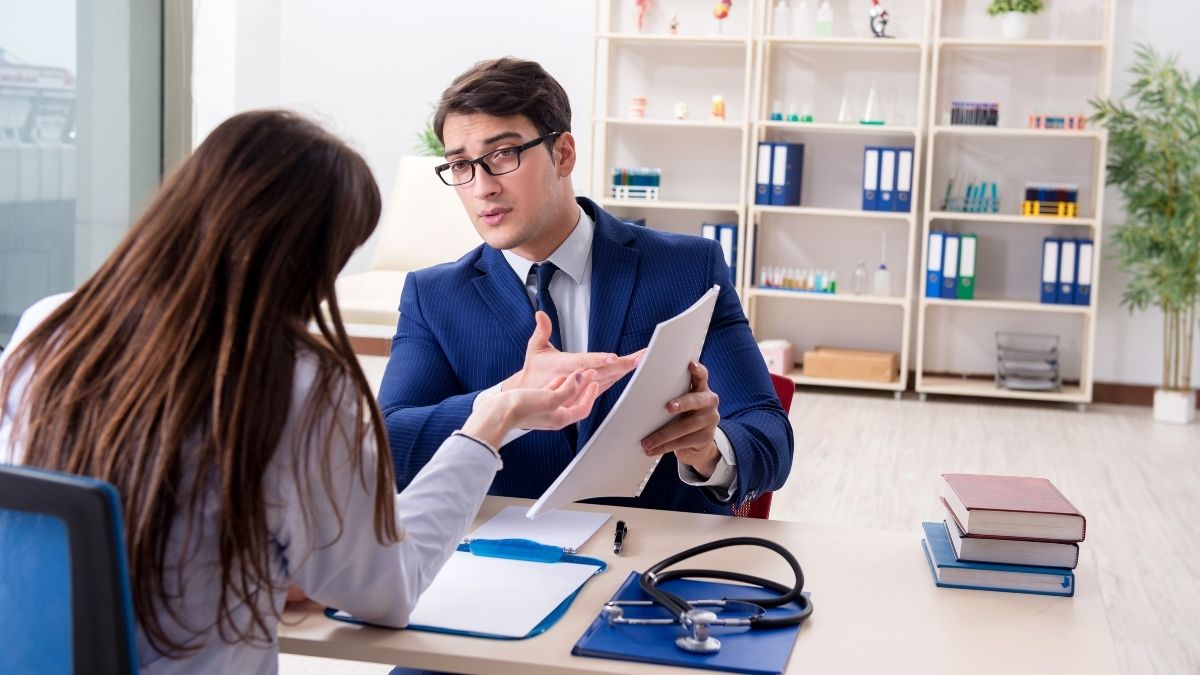 A man in a business suit explaining documents to a female doctor in an office setting, discussing the topic "does health insurance backdate."