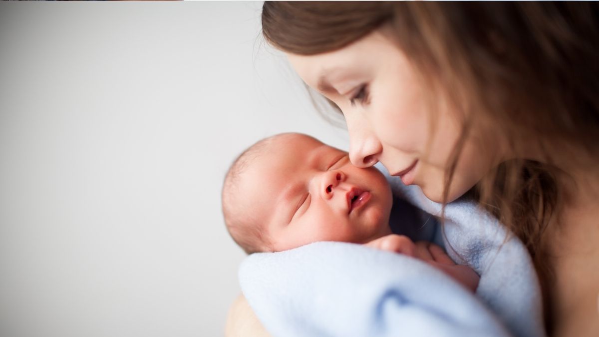 Mother lovingly holding newborn baby wrapped in a blanket, representing the importance of health insurance for newborns.