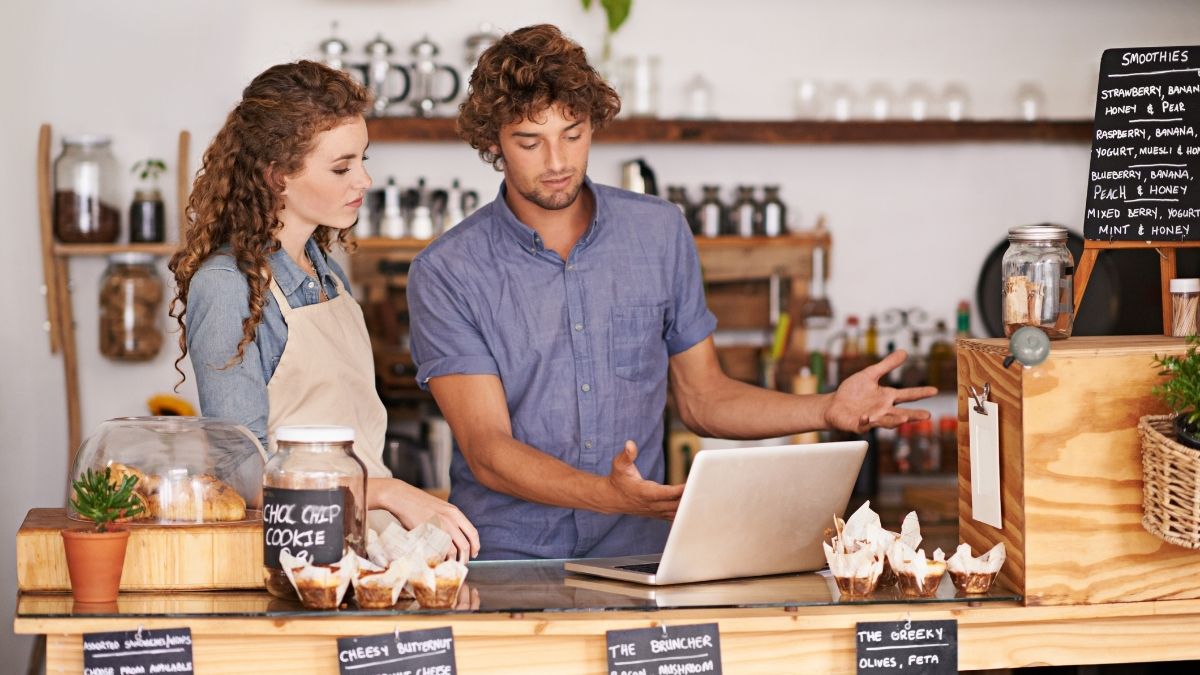 Small business owners discussing options on a laptop inside their café, representing the search for the best health insurance for small business.