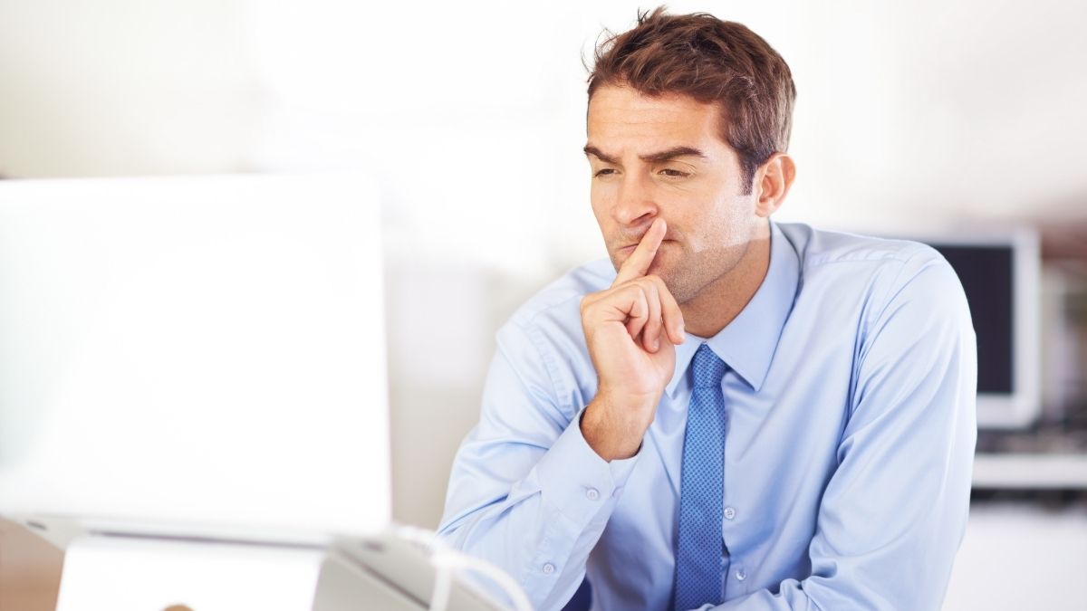 Man in business attire thinking while looking at a computer screen, representing financial planning and the question can I use HSA for DPC.