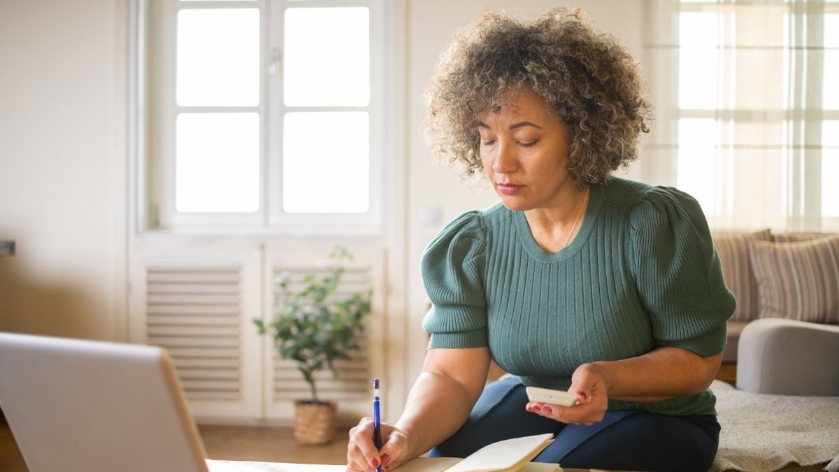 Focused woman reviewing medical bills and taking notes at home while learning about her health insurance out-of-pocket maximum.